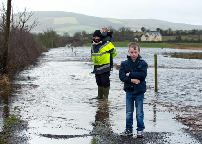 Rory Moloney with his eight-year-old twins, Caoimhe and Jack, at the completely submerged roadway to their home near O’Callaghans Mills. His wife and kids have had to leave the family home due to the flooding but Rory remains to look after his animals and farm.